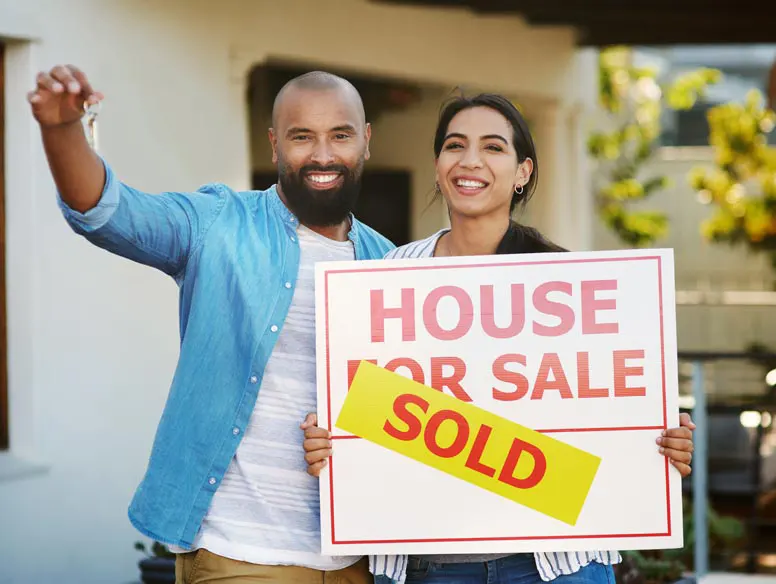 Latin couple standing in front of home with sold sign