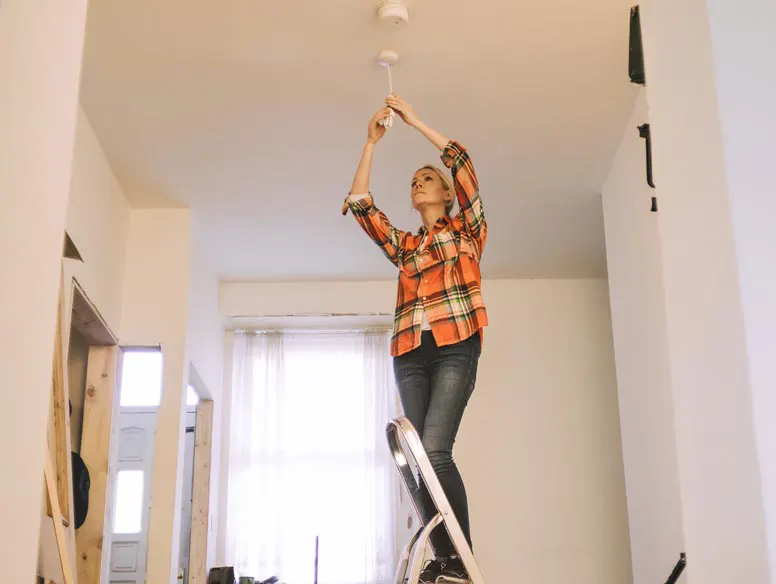 Woman on ladder repairing light fixture